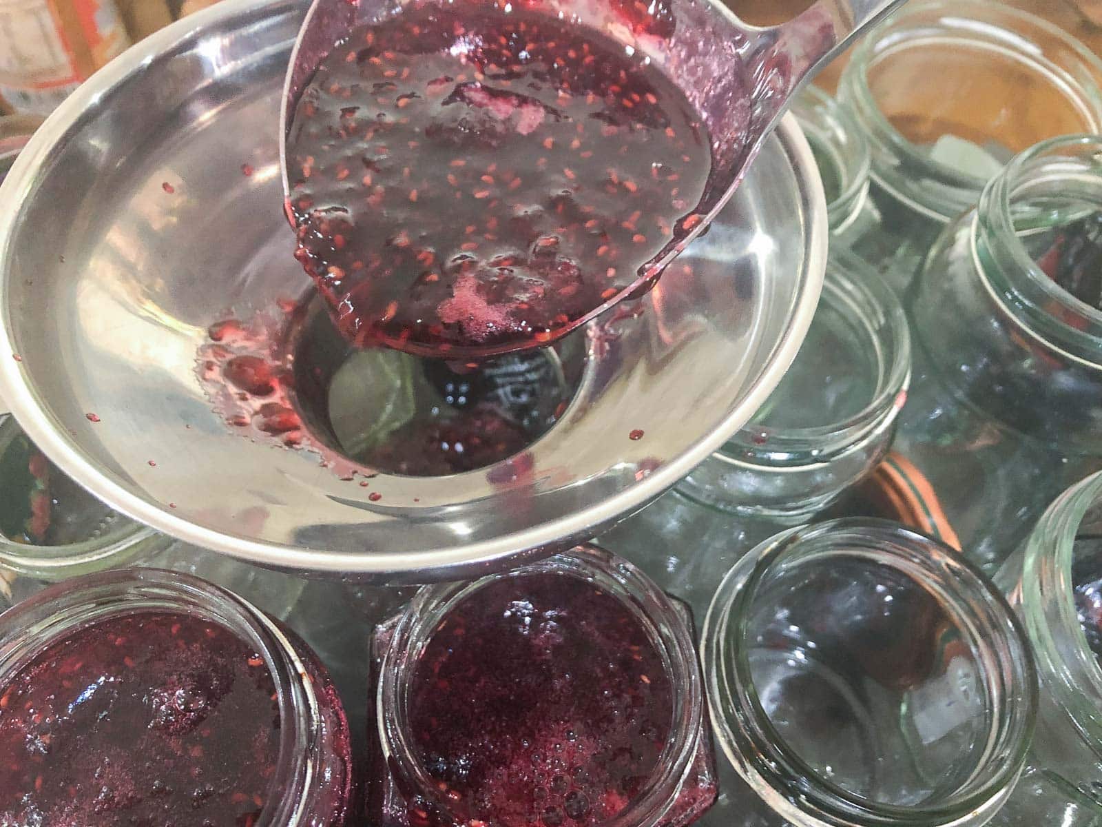 Spooning hot raspberry jam into sterilised jars.