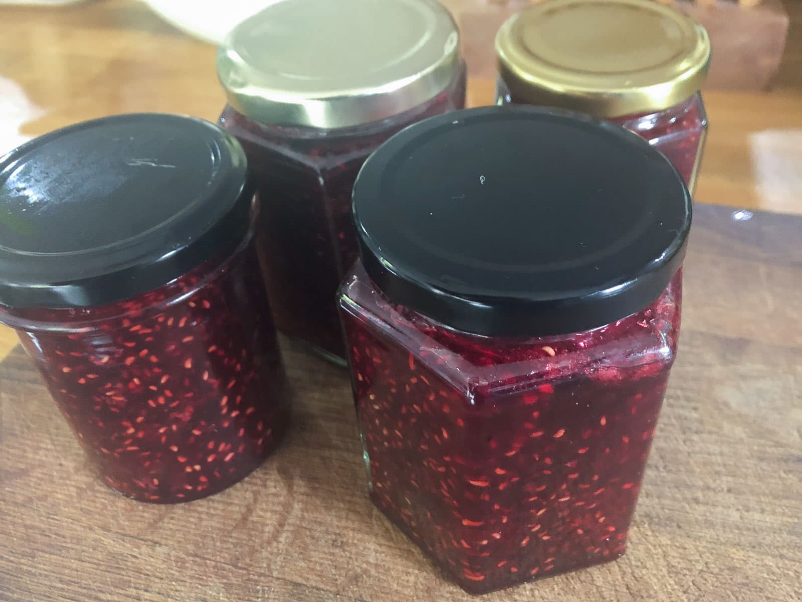 four jars of fresh homemade raspberry jam sitting on a wooden chopping board.