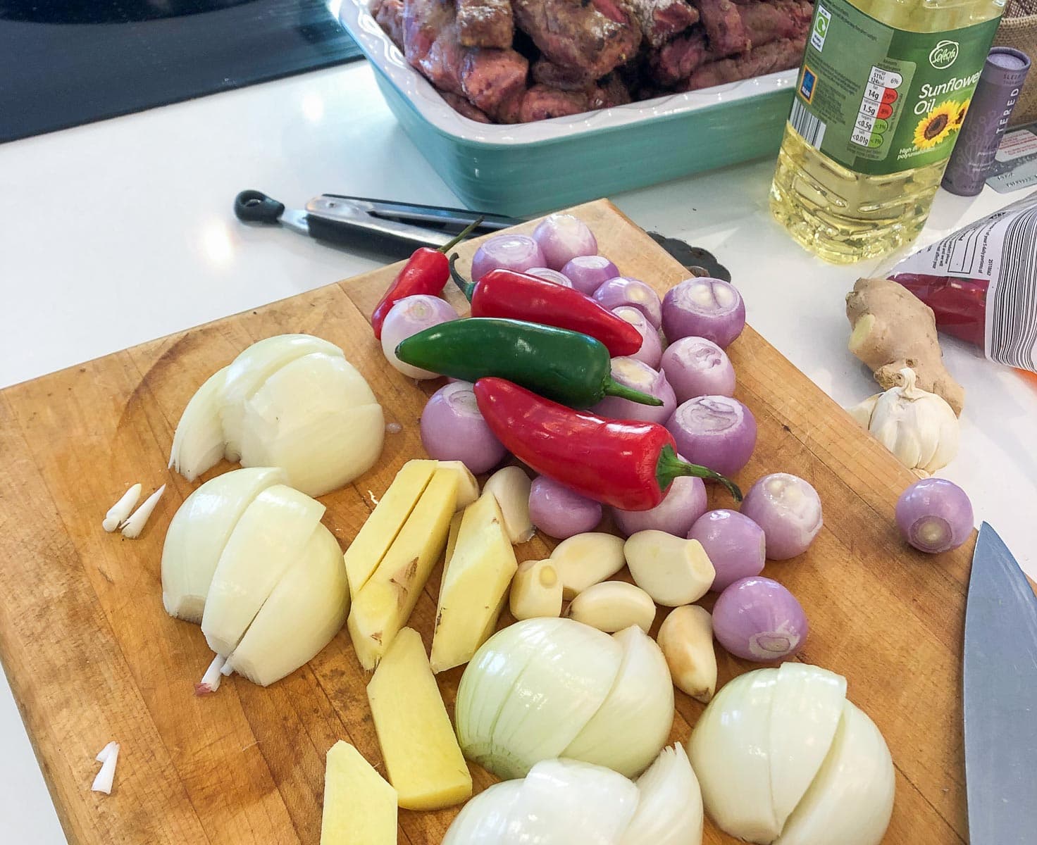 A wooden chopping board containing chopped vegetables like onions, ginger, shallots, chilies and garlic.