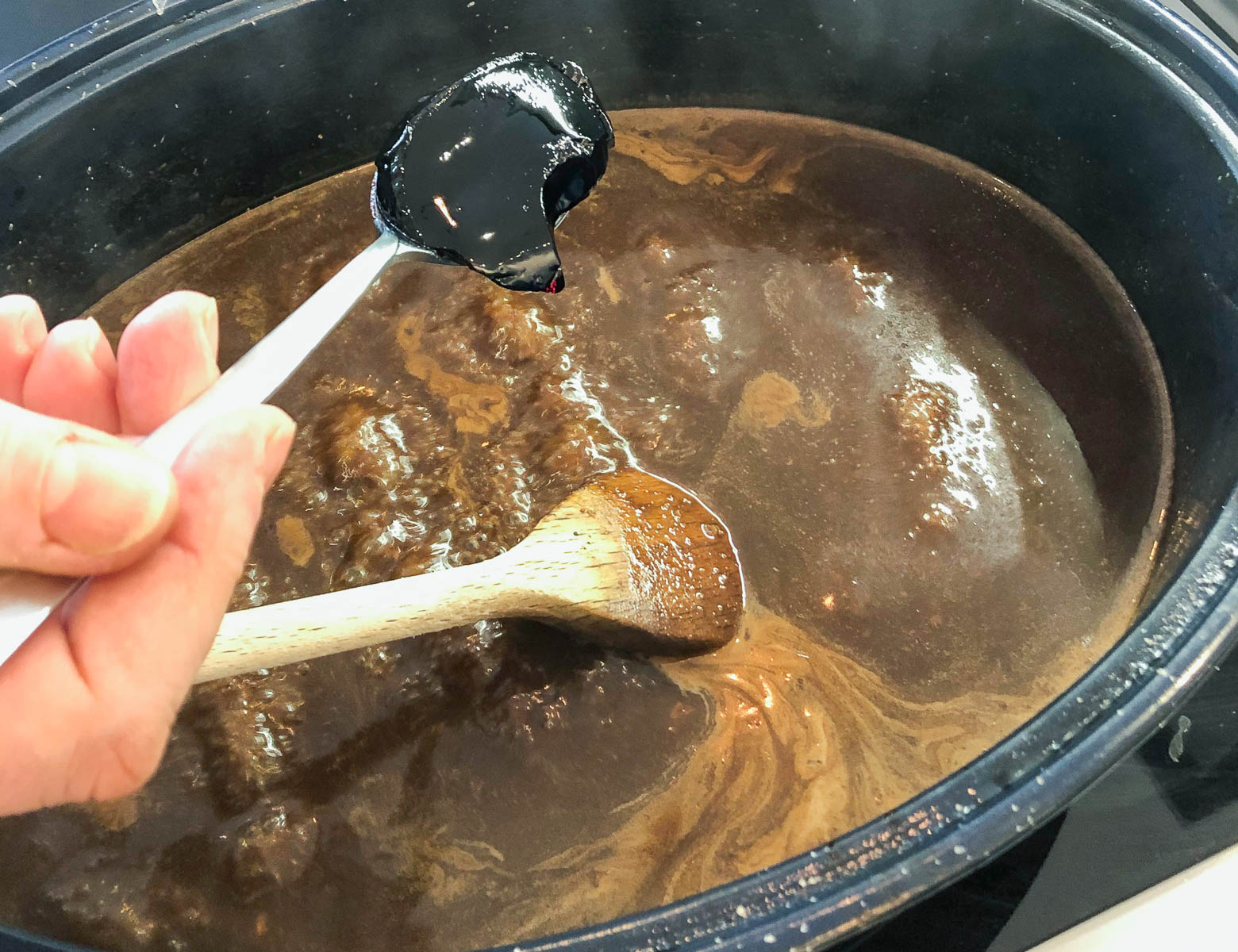 beef gravy reducing in a large pan with a spoon of blackcurrant jelly being added.