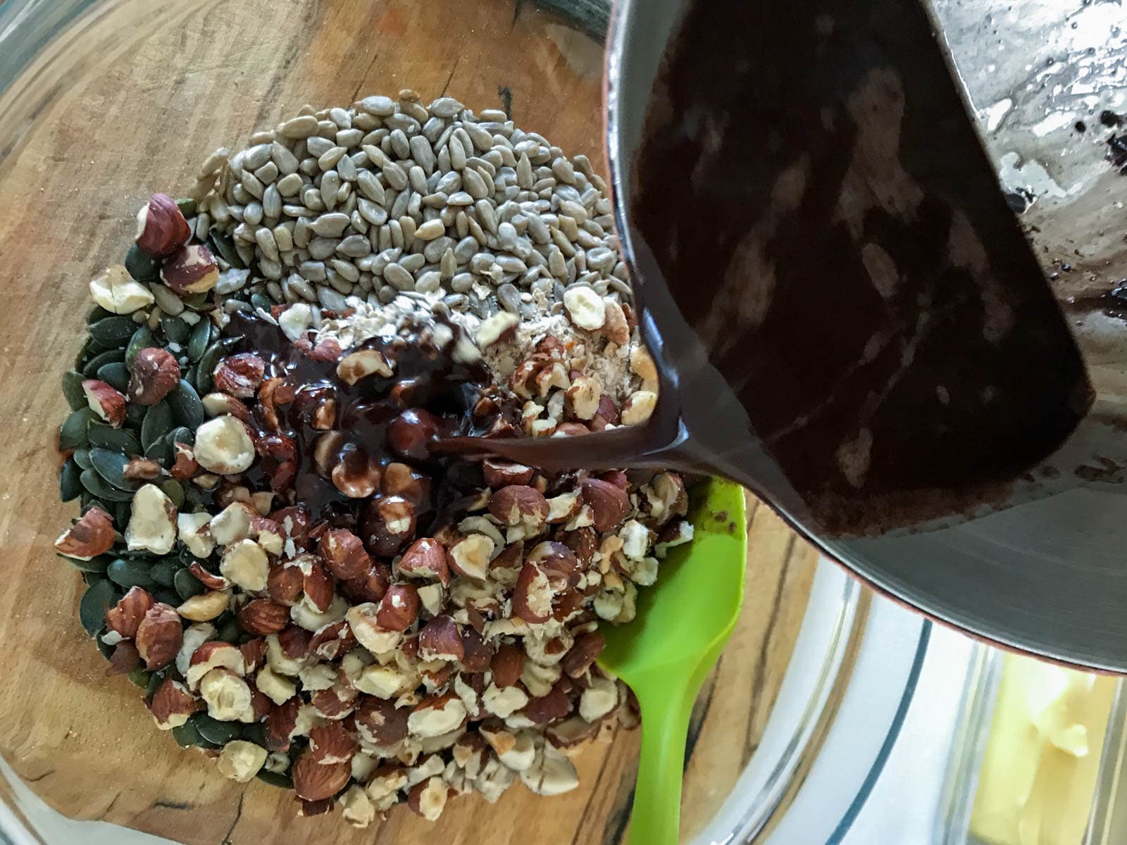 Pouring warm coconut oil, and chocolate over oats and nuts mixture to make granola.