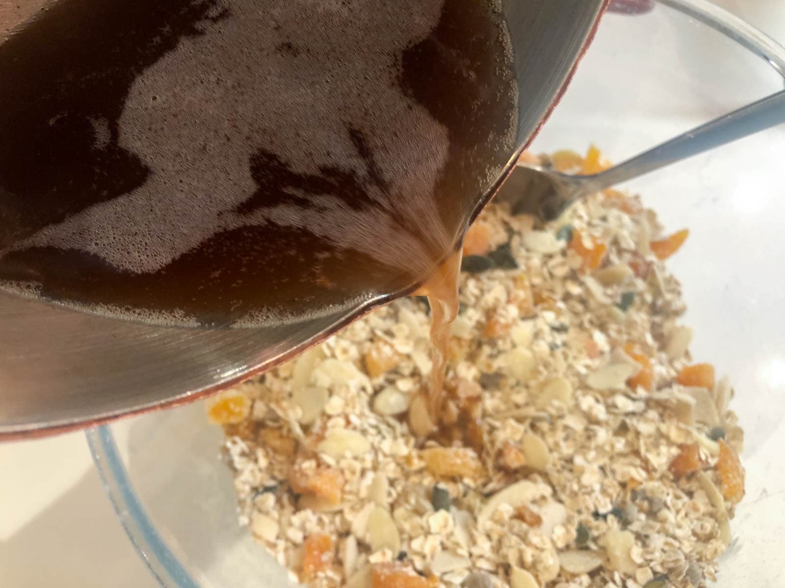 Pouring oil, spices and sugars over dried ingredients to make granola.