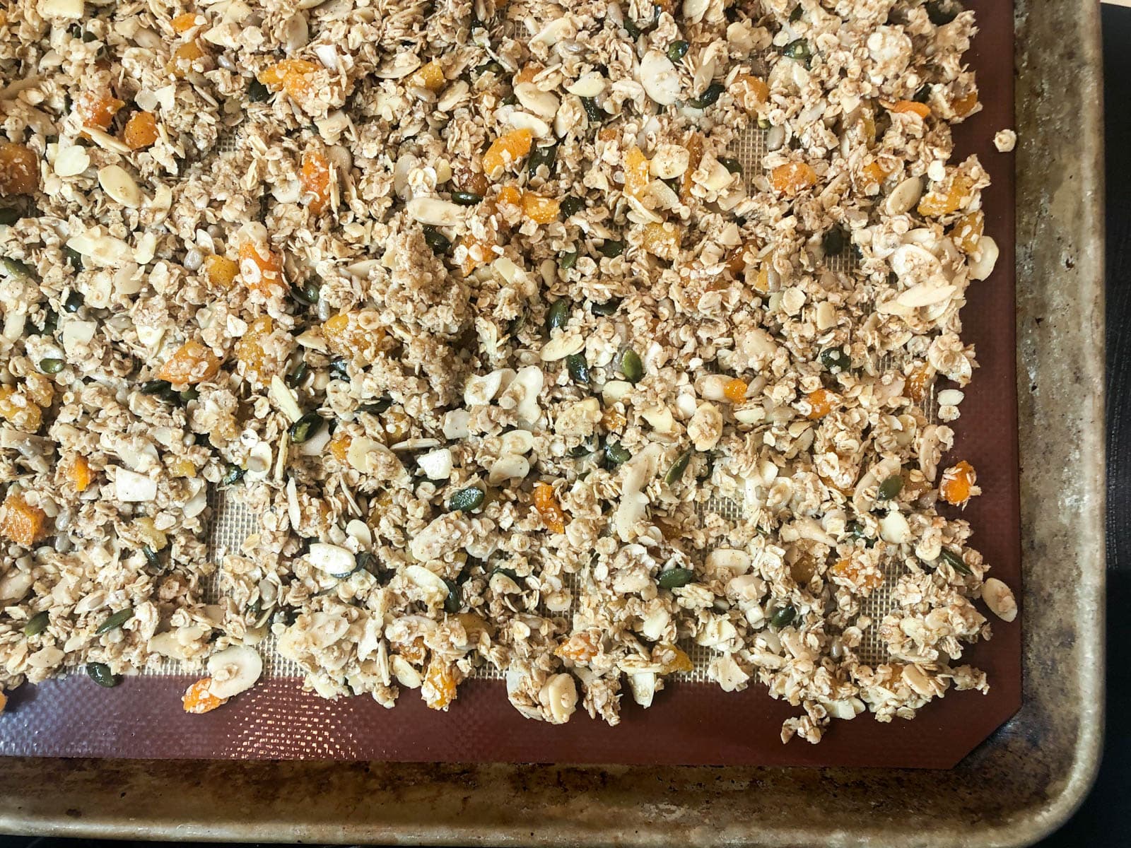 Uncooked granola on a baking tray with a silicon mat under.