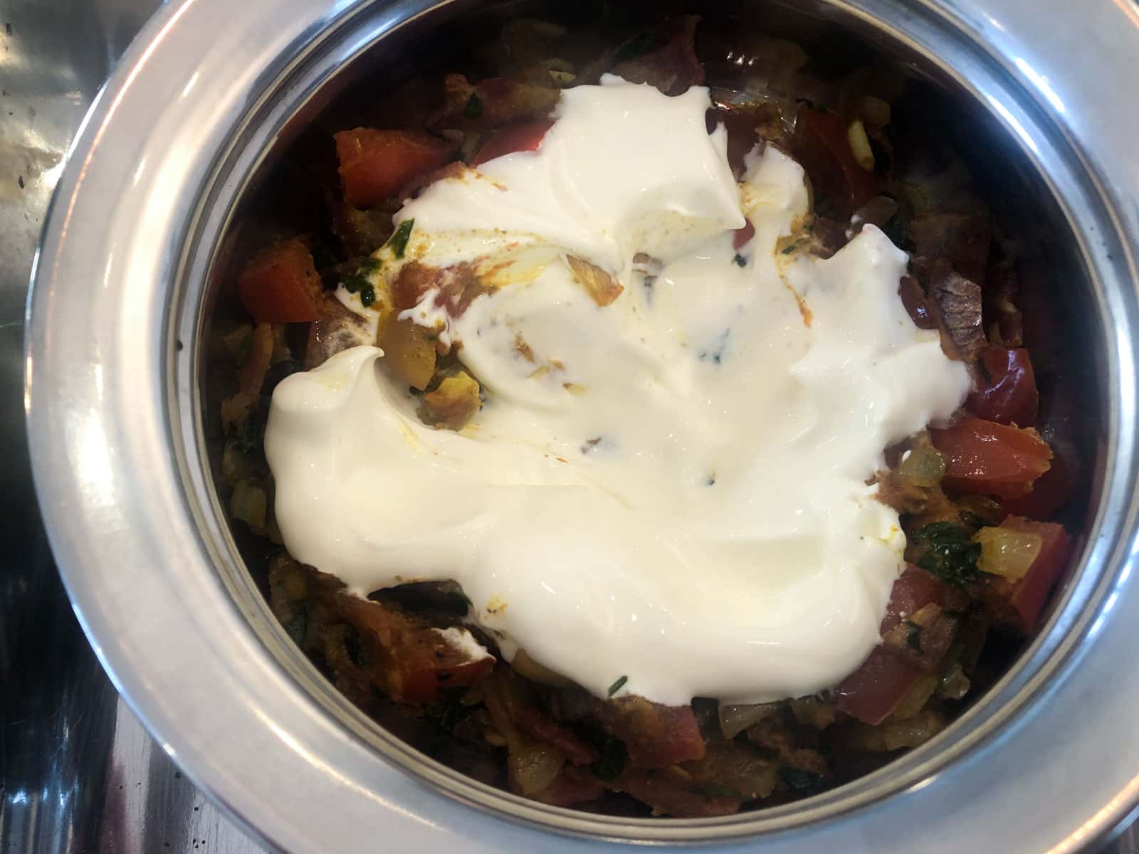 Curried vegetables topped with a large sppon of yogurt in a metal baking dish.