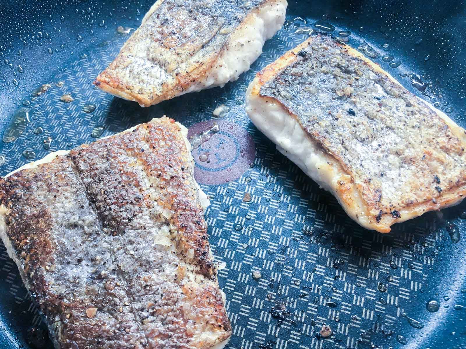 Crispy skined hake fillets in a hot frying pan.