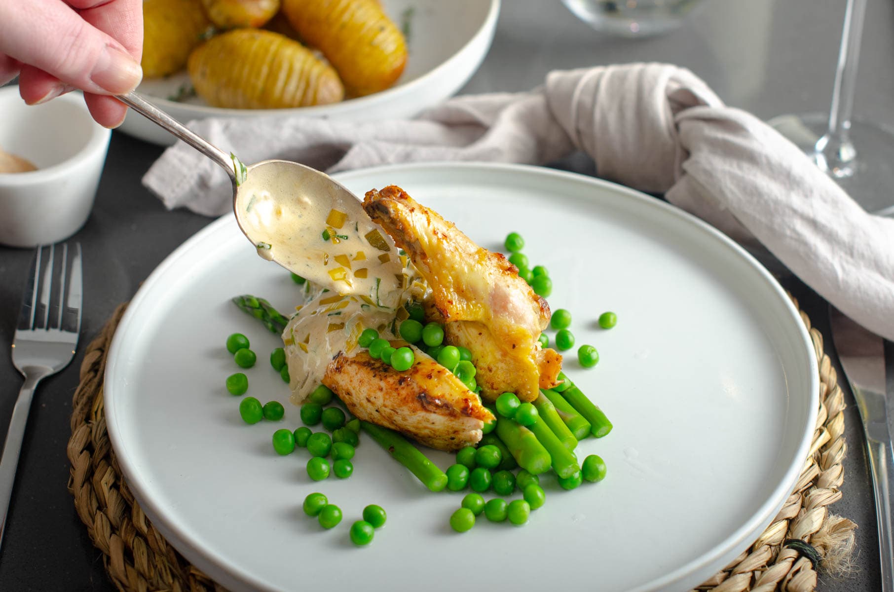 A creamy tarragon sauce being poured over tender chicken breasts served on a bed of fresh asparagus and spring peas on a white plate in a CALA Homes Showhome.