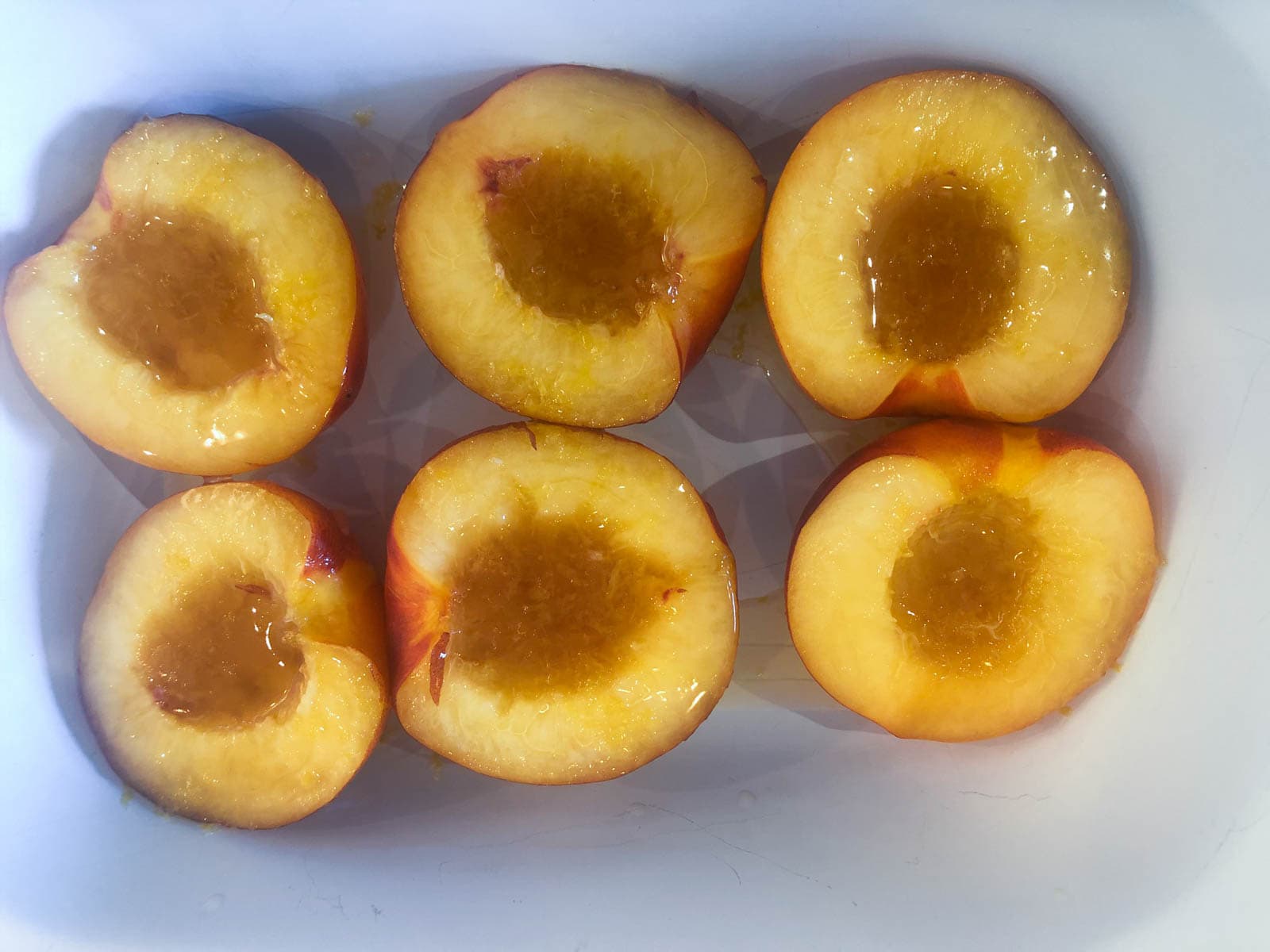 Nectarines halved and in a baking tray with lemon juice and maple syrup drizzled over.