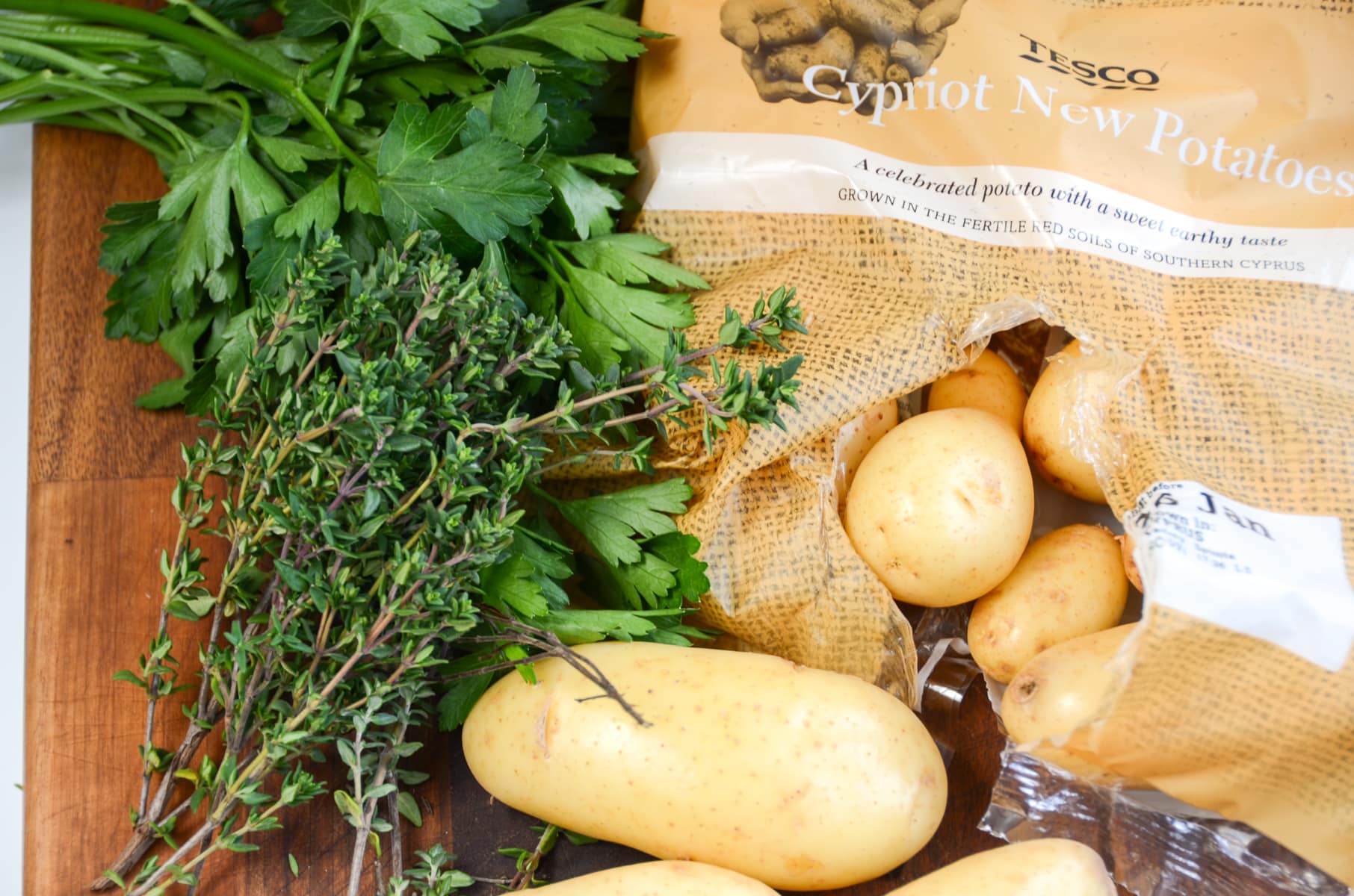 Fresh herbs including thyme and parsley with an open bag of Cypriot Potatoes.