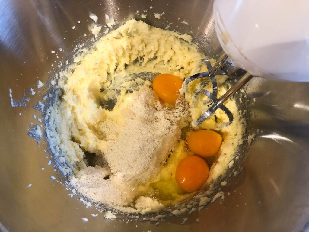A bowl mixing butter, sugar and ground almonds with added eggs.