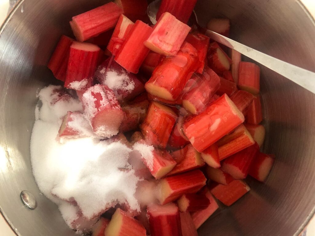 Chopped rhubarb stalks with sugar and a little water in a pan.