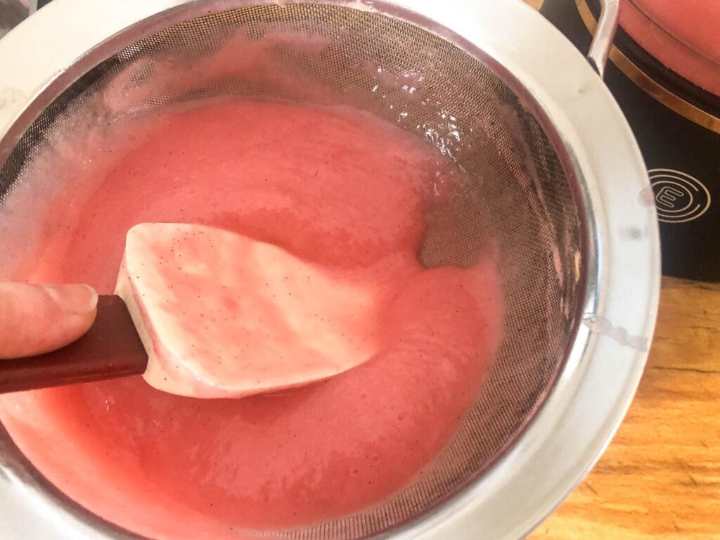 Rhubarb puree being passed through a mesh sieve to extract the juice.