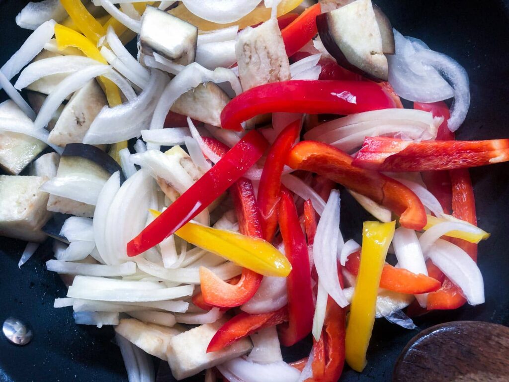 Sliced onions and peppers with diced aubergine ready to cook down as a base for adding eggs for a baked dinner.
