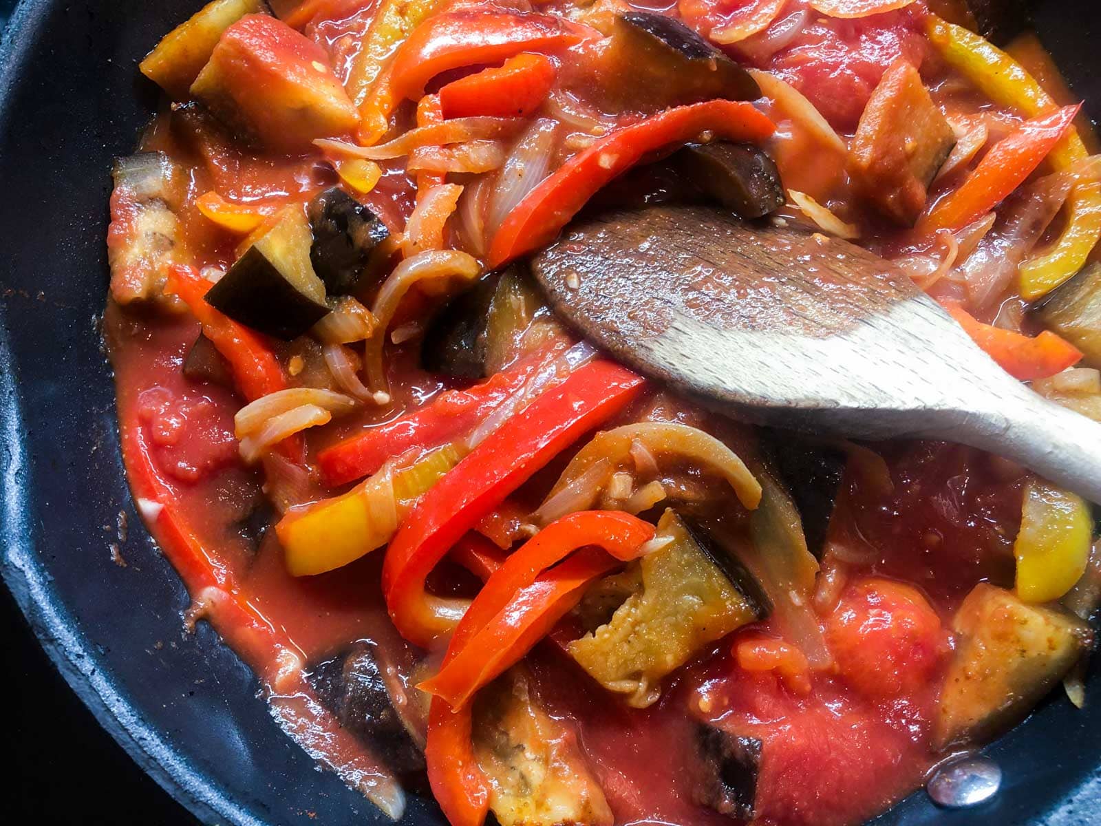 Peppers, onions and aubergines cooking in a fry pan with spices and tomatoes.