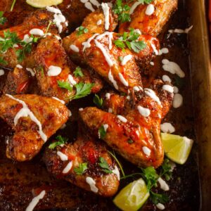 Spicy oven baked chicken wings on a tray drizzled with lime crema, hot sauce and fresh coriander.