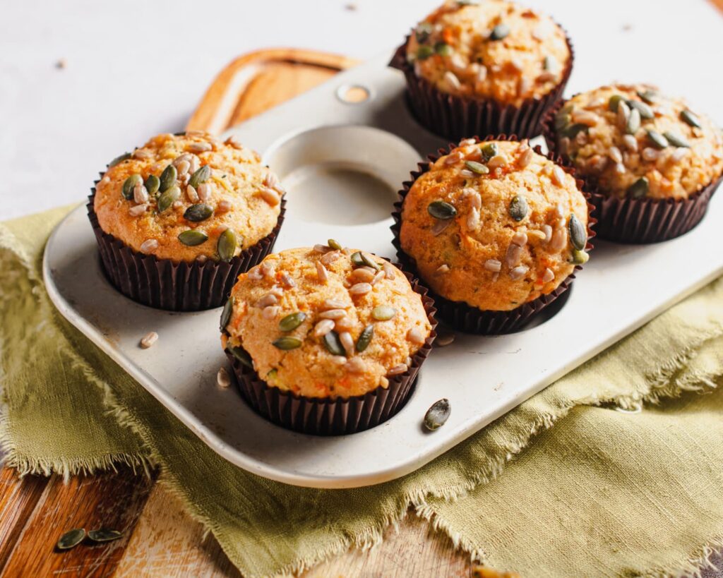 Breakfast muffins in a tray topped with seeds on a wooden board.