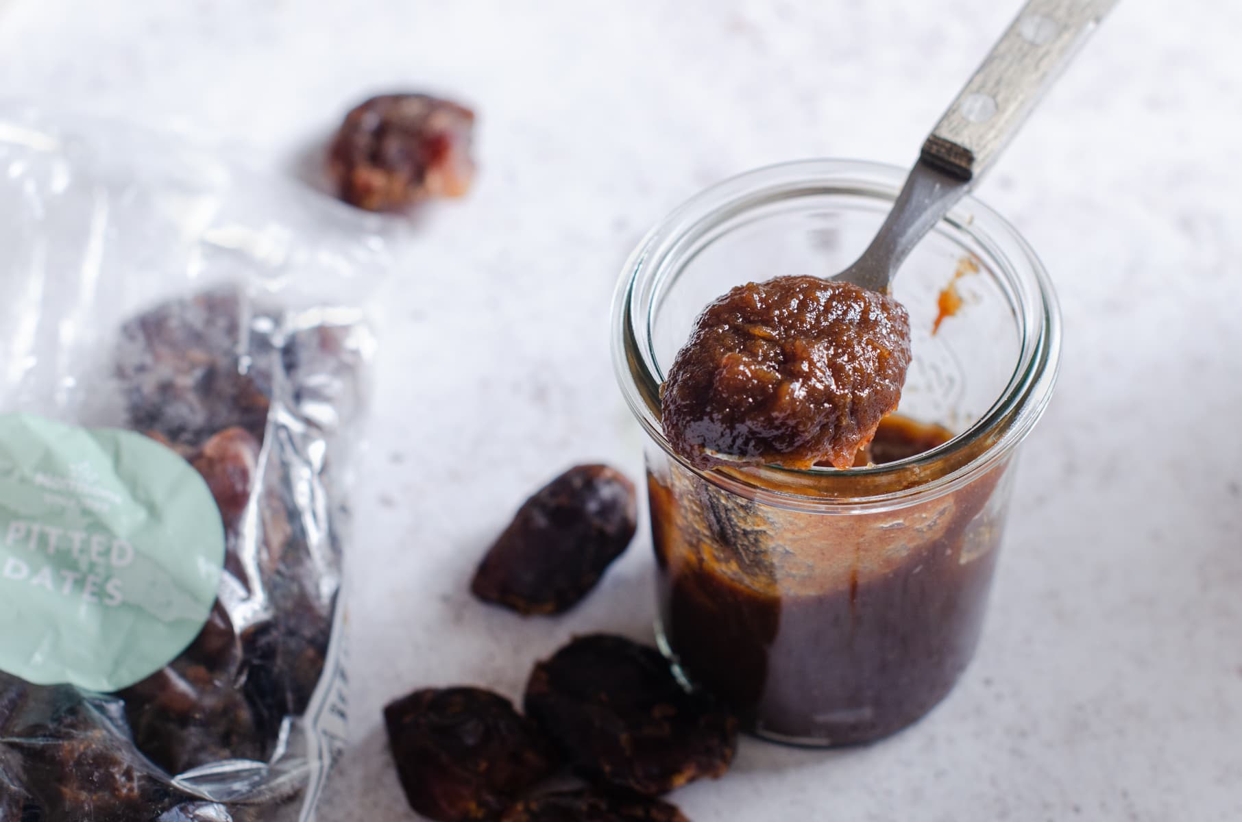 A glass jar of fresh made date and tamarind chutney with some dates scattered.