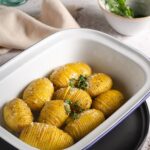 A bowl of hasselback potatoes with fresh thyme to the back.