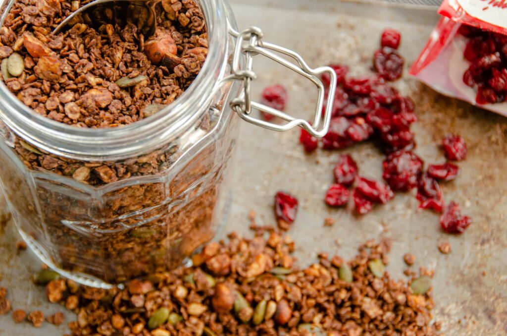 A jar of homemade granola with hazelnuts and dried cranberries, with some spilled out.