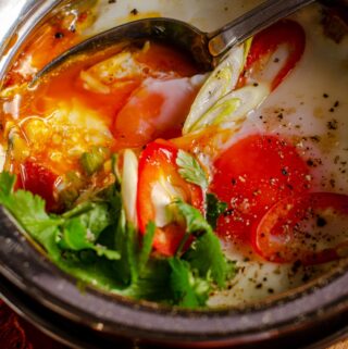 Eggs baked in a curry dish with a curry base and topped with fresh herbs.