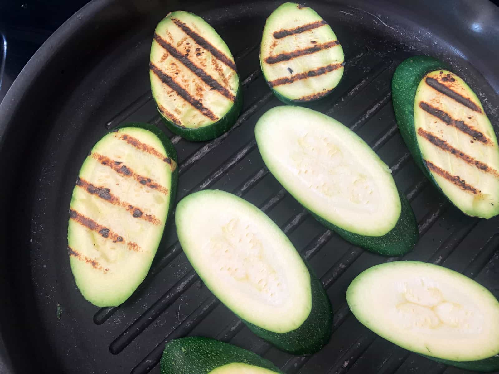 Slices of courgettes grilling in a pan.