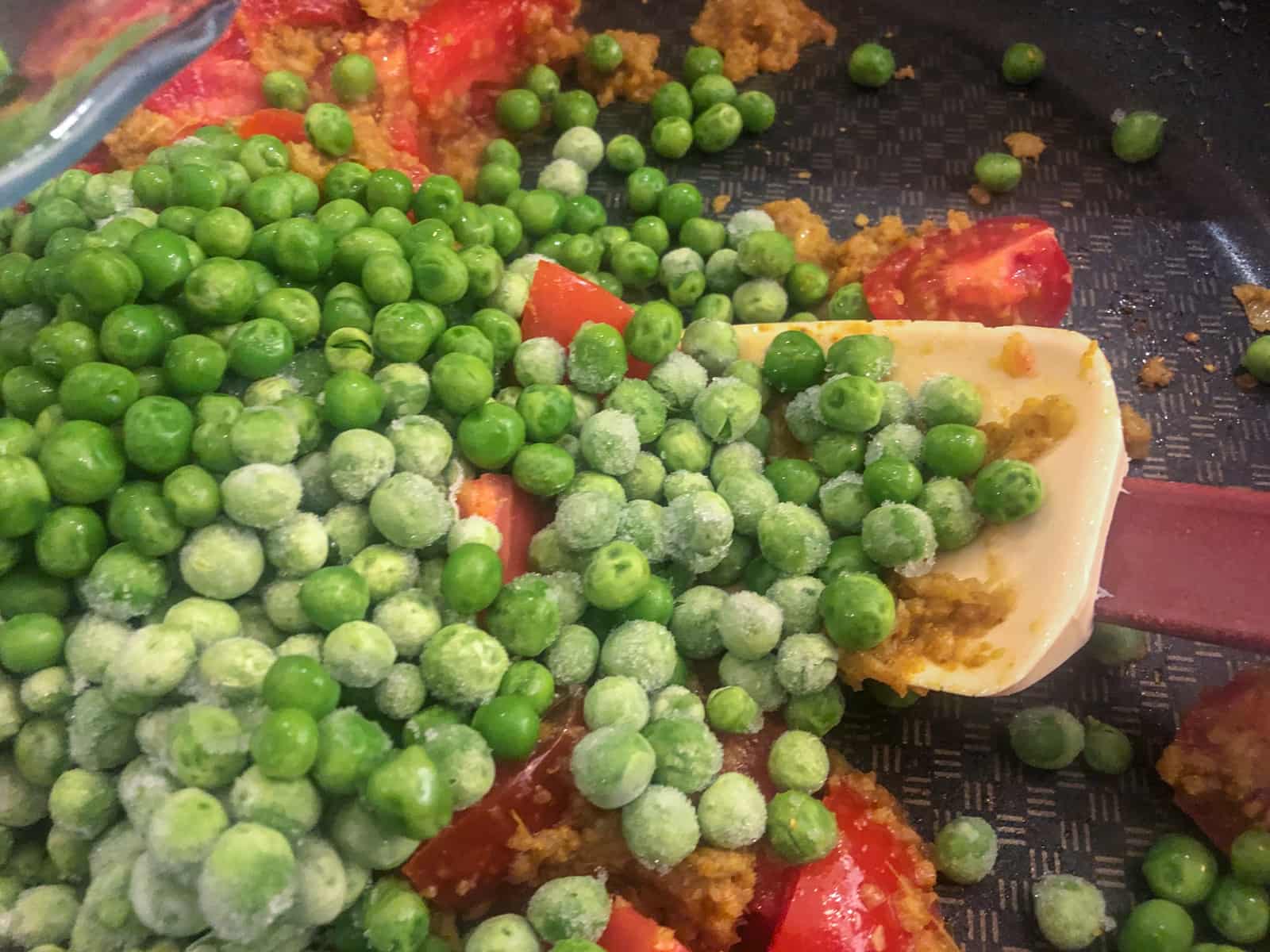 Frozen peas added to a curry paste and tomatoes in a skillet.