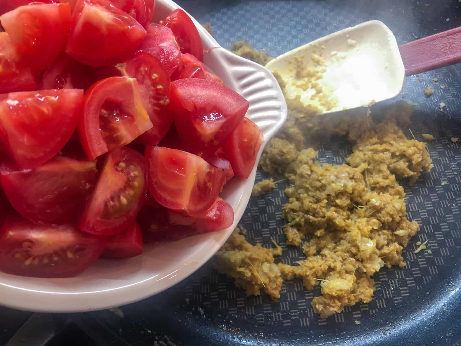 Fresh tomatoes being added to a skillet cooking a curry paste.