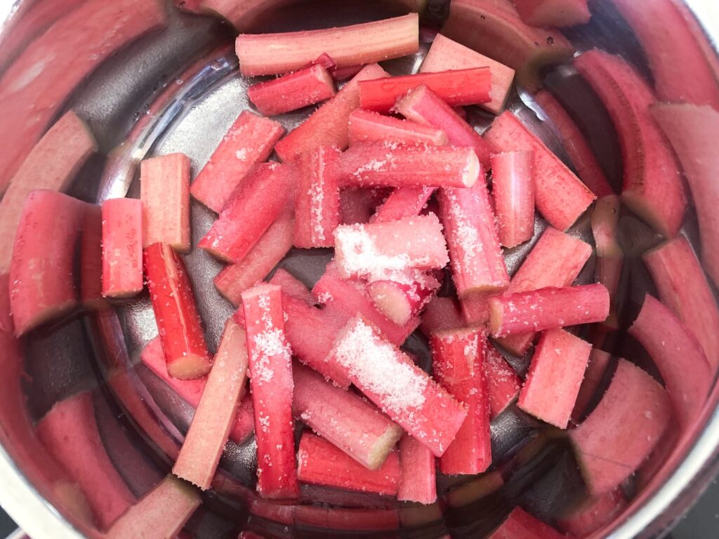 Stalks of fresh tender rhubarb in a pan and some sugar added to give a slight sweetness.