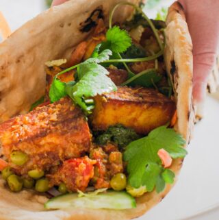 A hand wrapped up a fresh homemade flatbread filled with a paneer curry and chutneys.