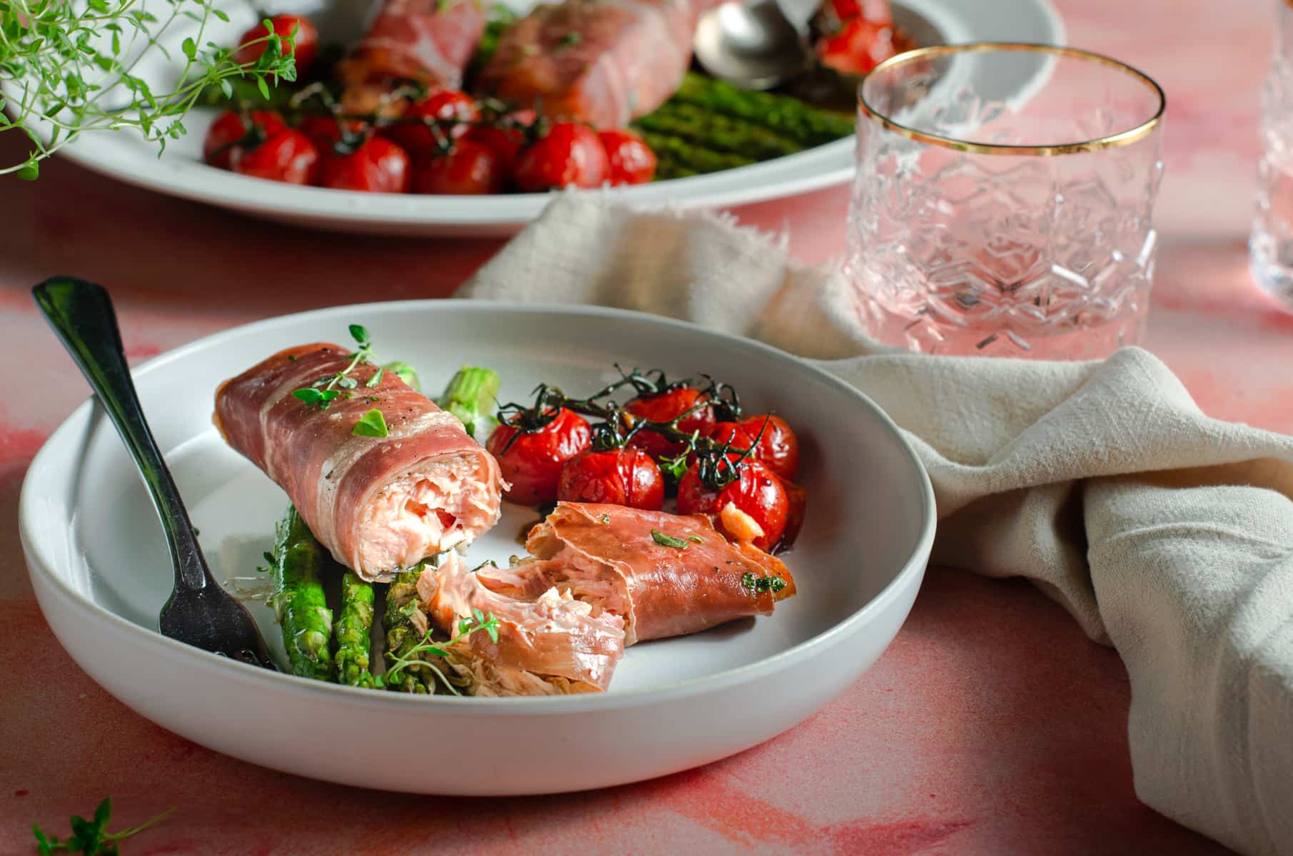 A serving suggestion for salmon wrapped in parma ham with asparagus and roasted tomatoes.