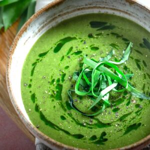 A close up image of wild garlic soup drizzles with wild garlic oil and topped with shredded wild garlic leaves.
