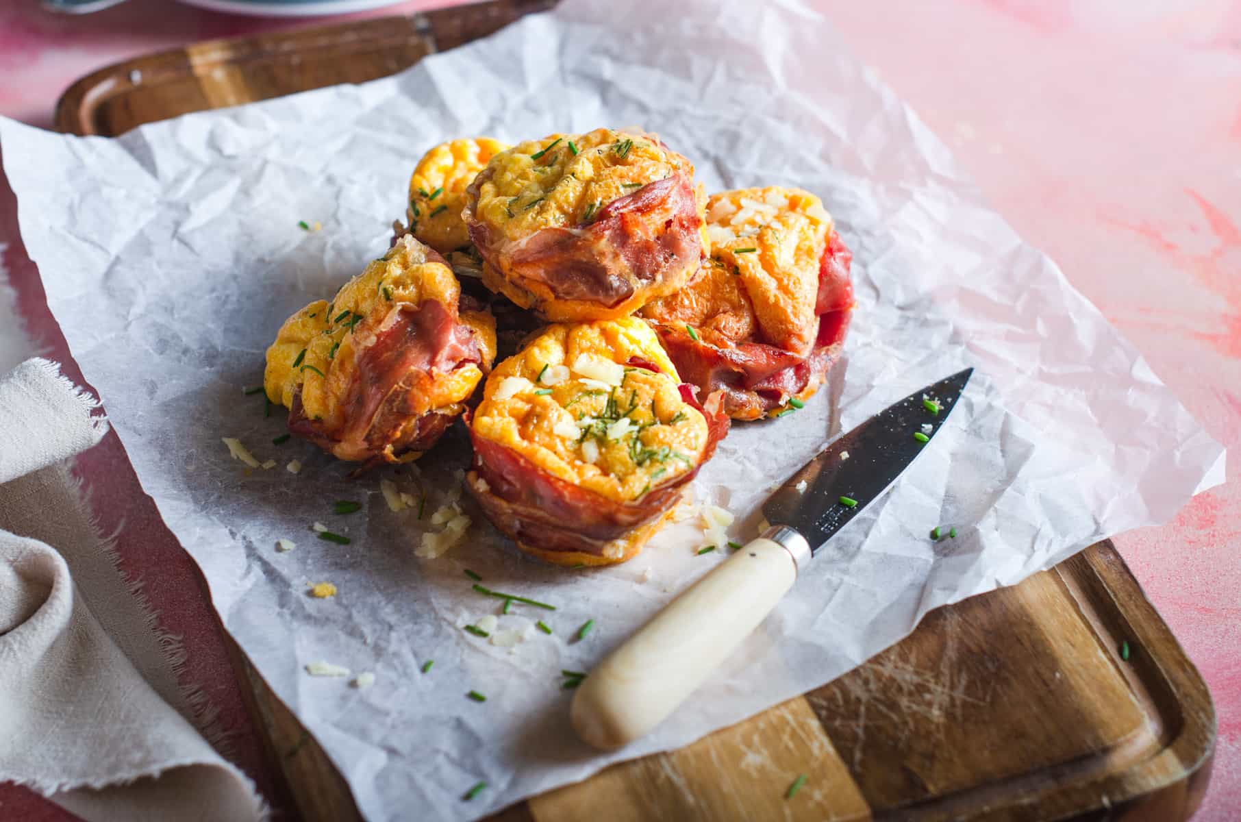 Parma ham and scrambled egg muffins piled on a wooden board for serving.