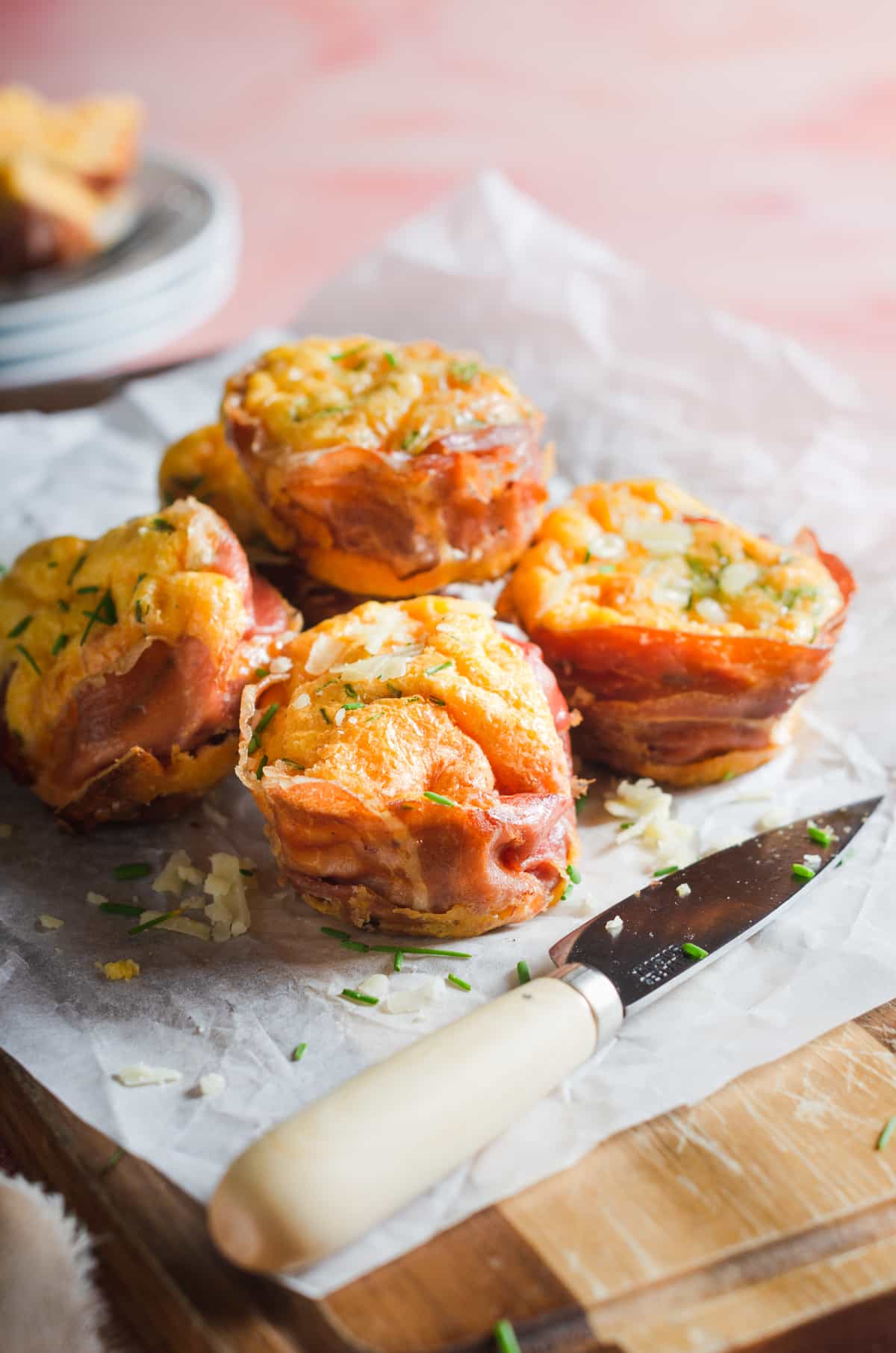 Bacon and egg muffin cups on a wooden board and with a knife sitting to the front.
