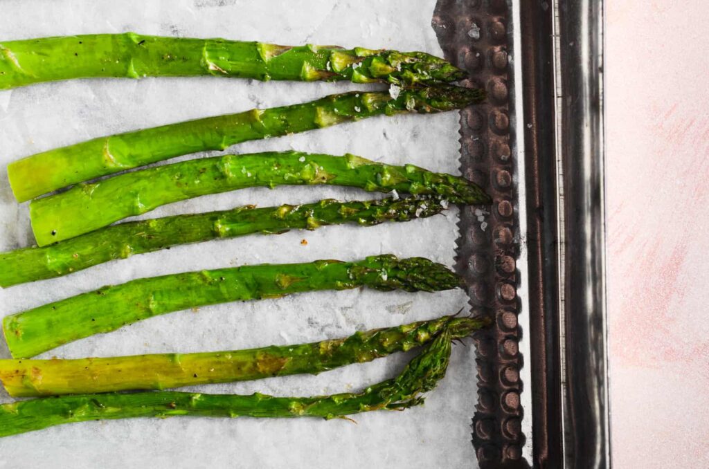 Oven roasted spears of tender asparagus on a baking tray just out of the oven.