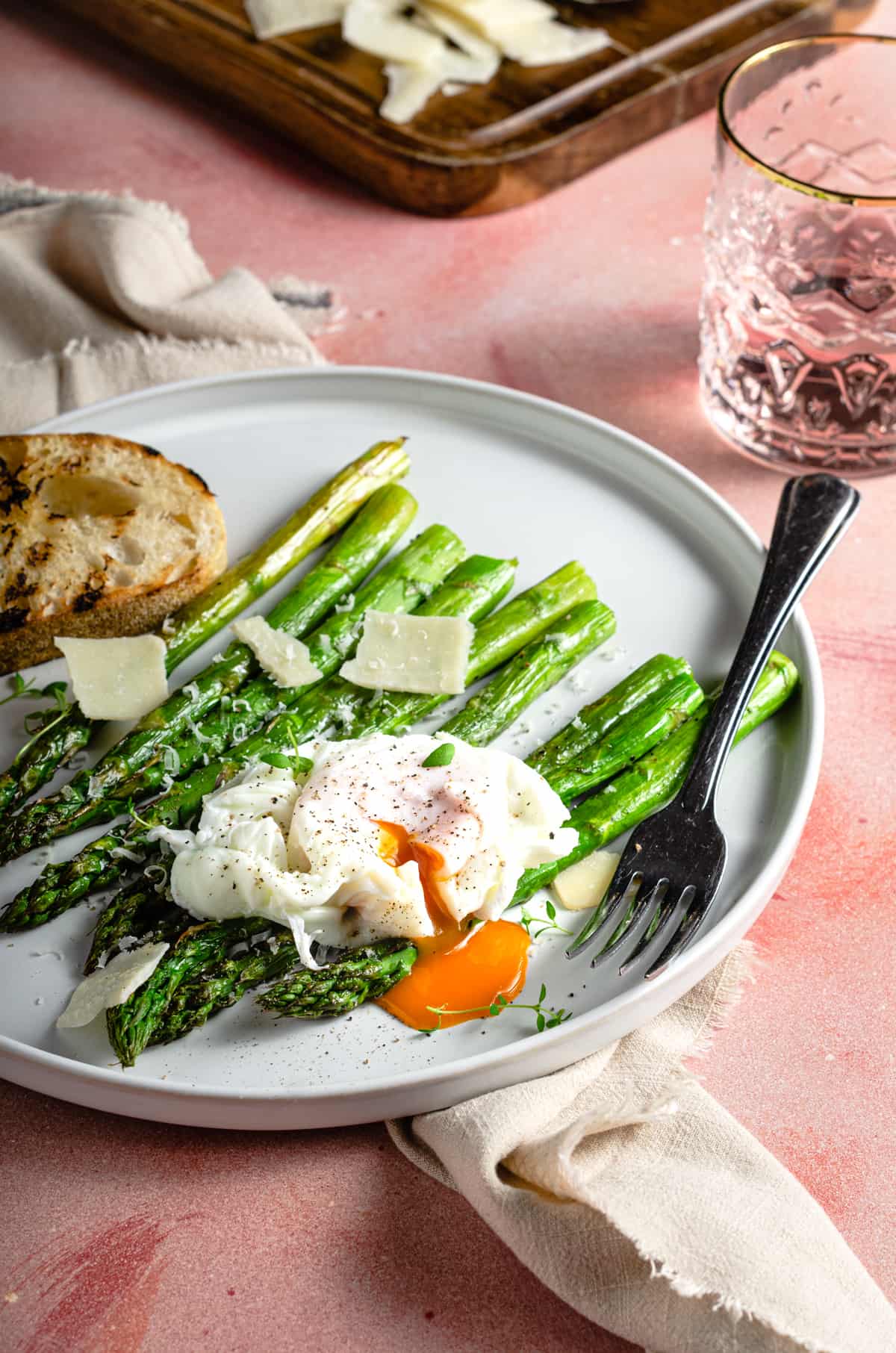 A brunch scene of roasted asparagus topped with a poached egg and shavings of parmesan cheese.