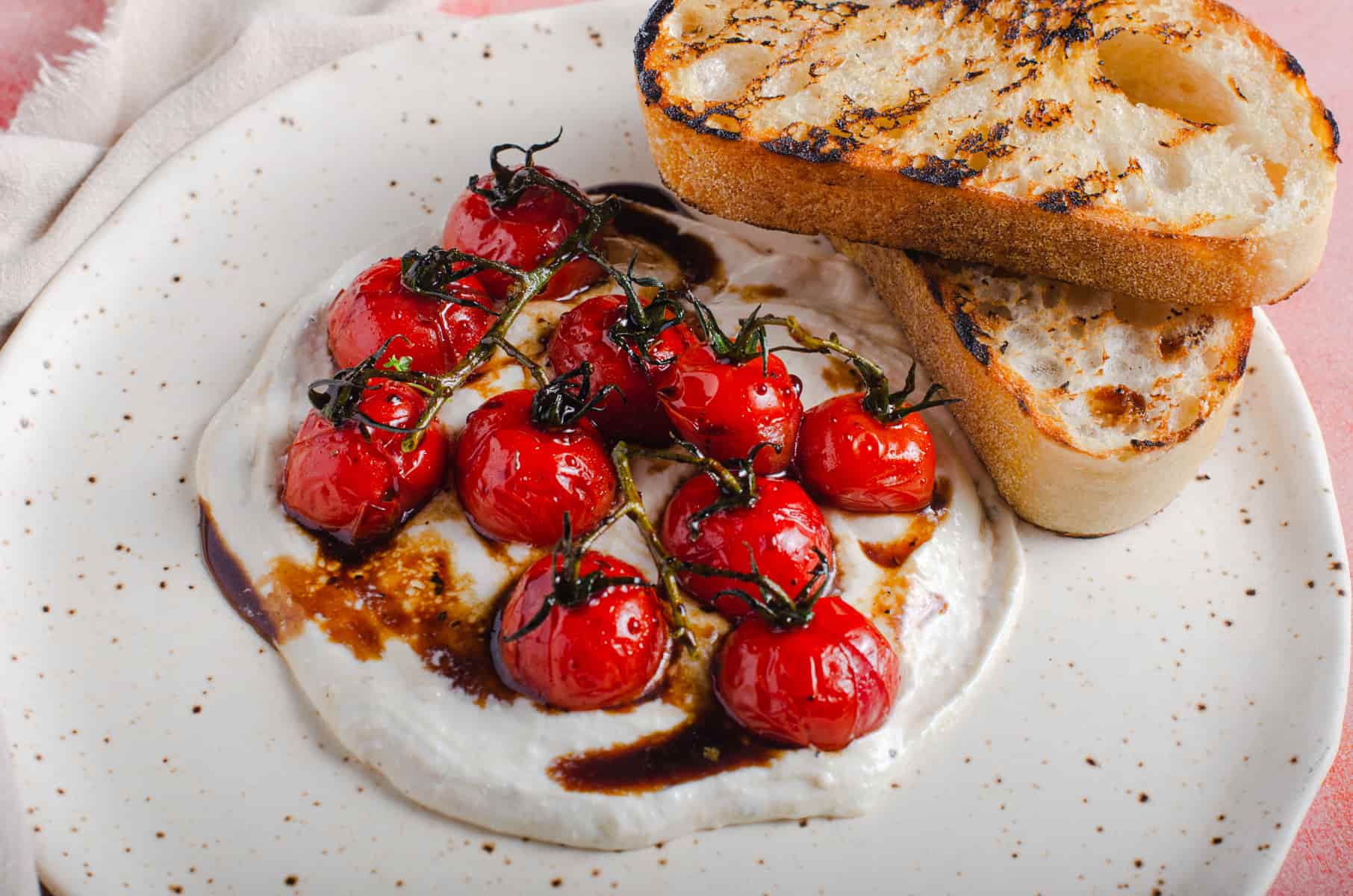 A speckled plate containing whipped feta cheese, oven roasted balsamic glazed vine tomatoes and toasted slices of sourdough bread.