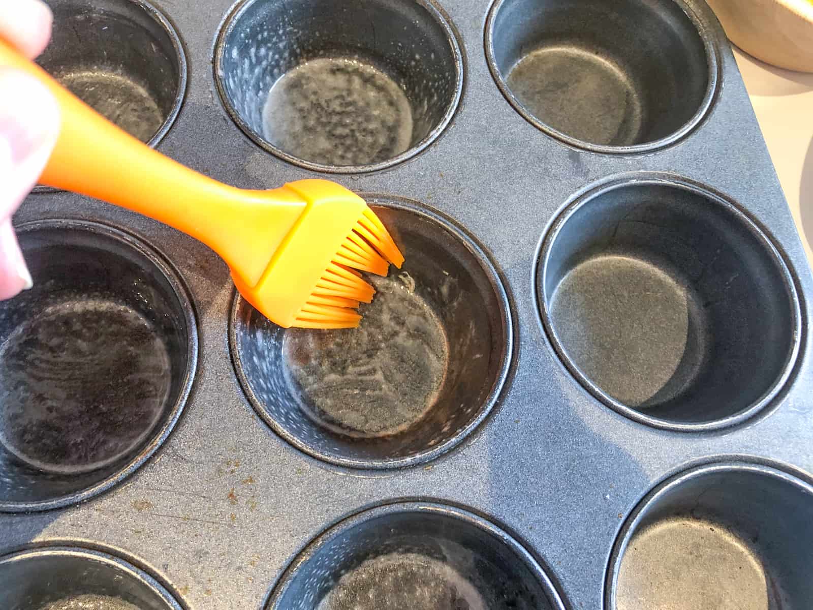 Using a silicone pastry brush to oil a muffin tray.