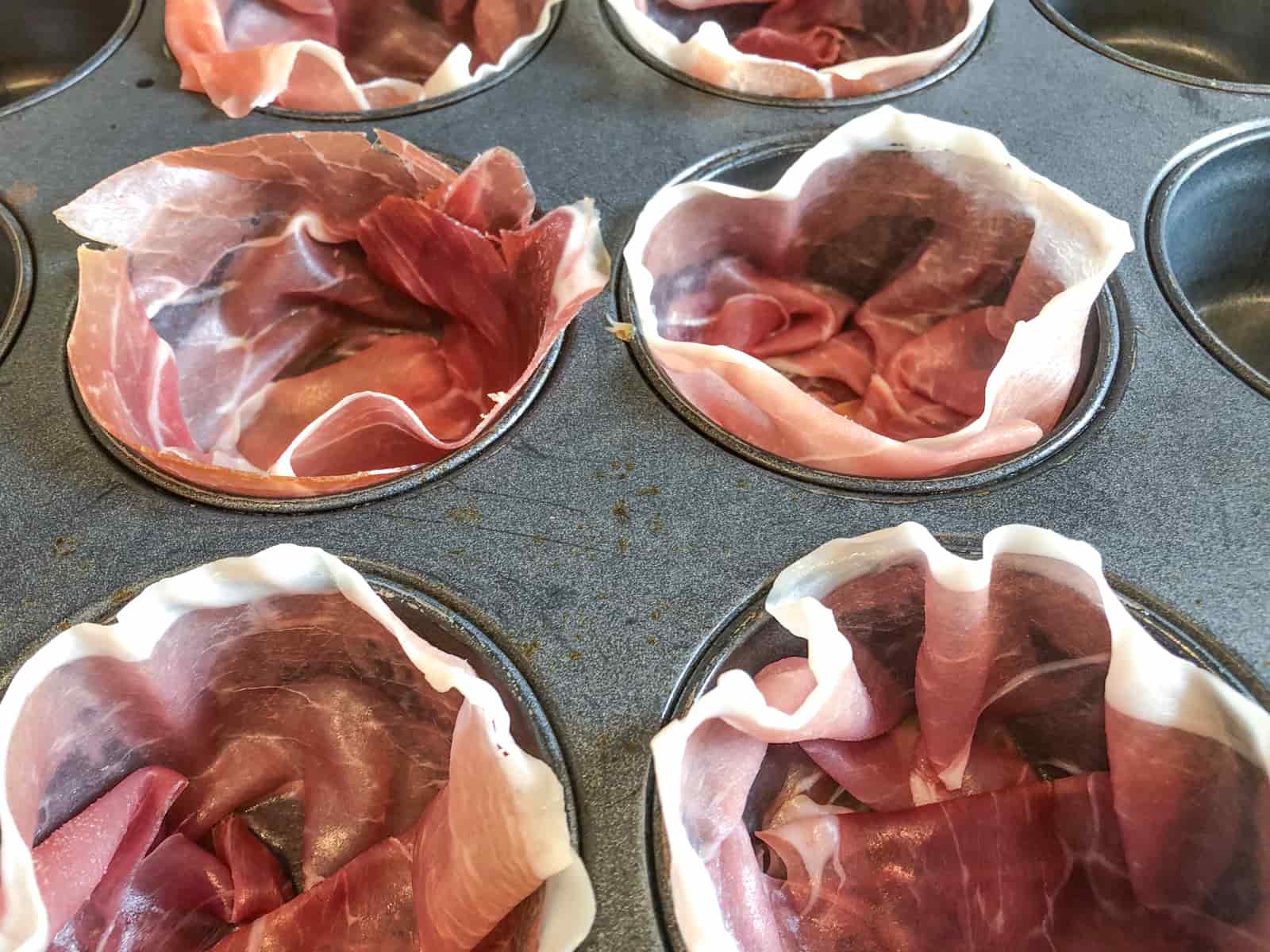 Slices of wafer thin parma ham lining a muffin tray to before eggs are added.