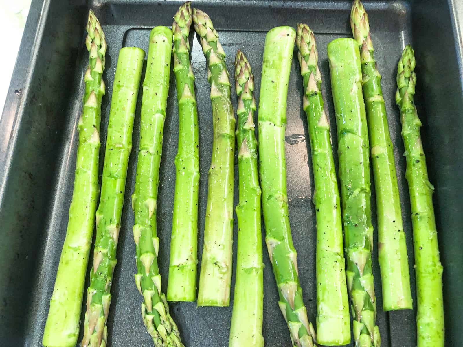 Asparagus spears on a baking tray about to be roasted.