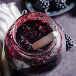 A jar of homemade blackberry jam with a spoon in the middle.