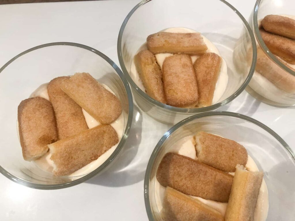 Small bowls with layered lemon cream and lady fingers.