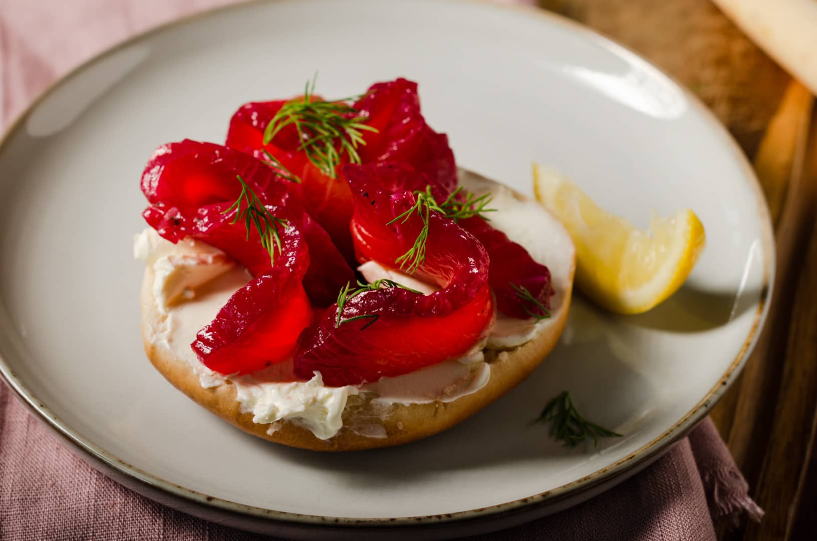 Beetroot cured salmon slices on a bagel with cream cheese and a slice of lemon wedge