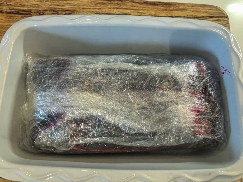 Tightly wrapped beetroot cured salmon in a baking dish before being refrigerated.