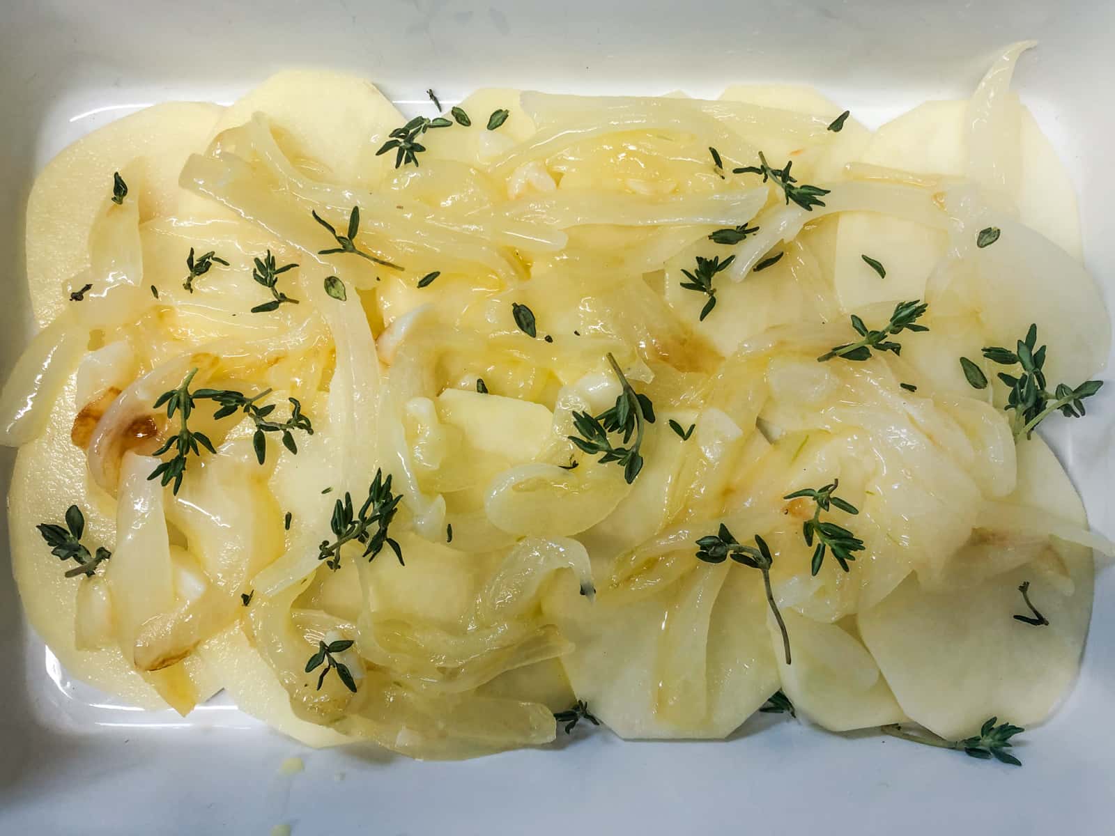 Sliced potatoes topped with cooked onions and garlic and fresh thyme.