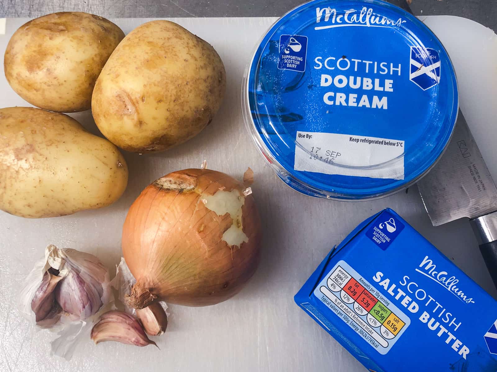 Ingredients for a potato gratin consisting of potatoes, garlic, onions, butter.