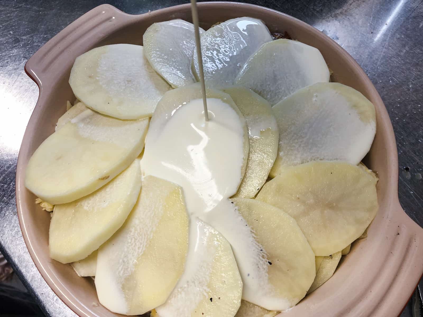 Pouring single cream over top of sliced potato gratin before baking.