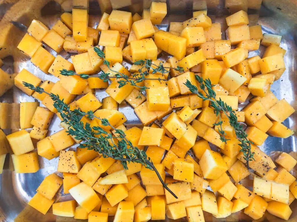 Diced butternut squash in a roasting tin seasoned and with fresh thyme stalks.