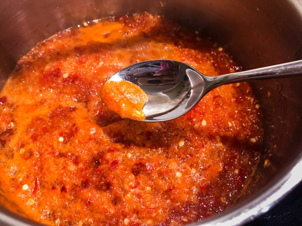 Showing a spoon skimming the surface of chilli jam whilst cooking to remove the scum from the surface to keep the jam translucent.