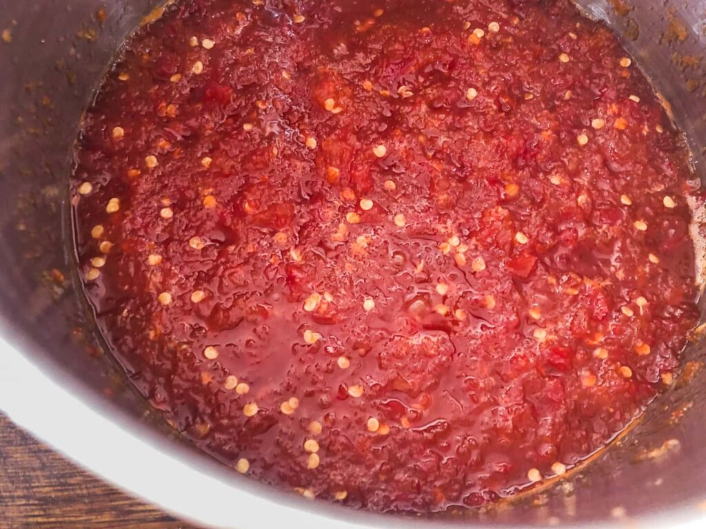 Showing how the chilli jam is cooking and starting to darken in colour as the sugar forms a syrup and thickens the jam.
