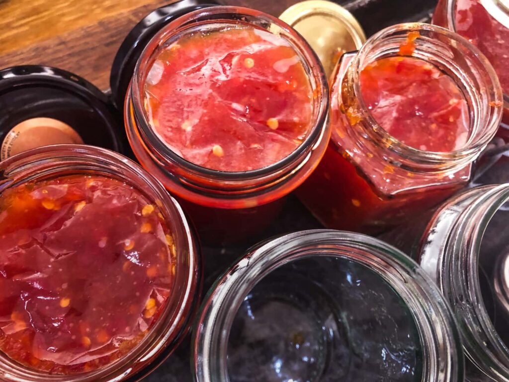 Chilli jam being filled into sterilised jars and topped with a wax disc to keep the air out.