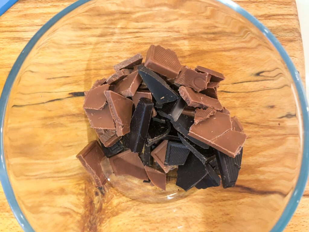 Pieces of milk and dark chocolate in a glass bowl broken up.